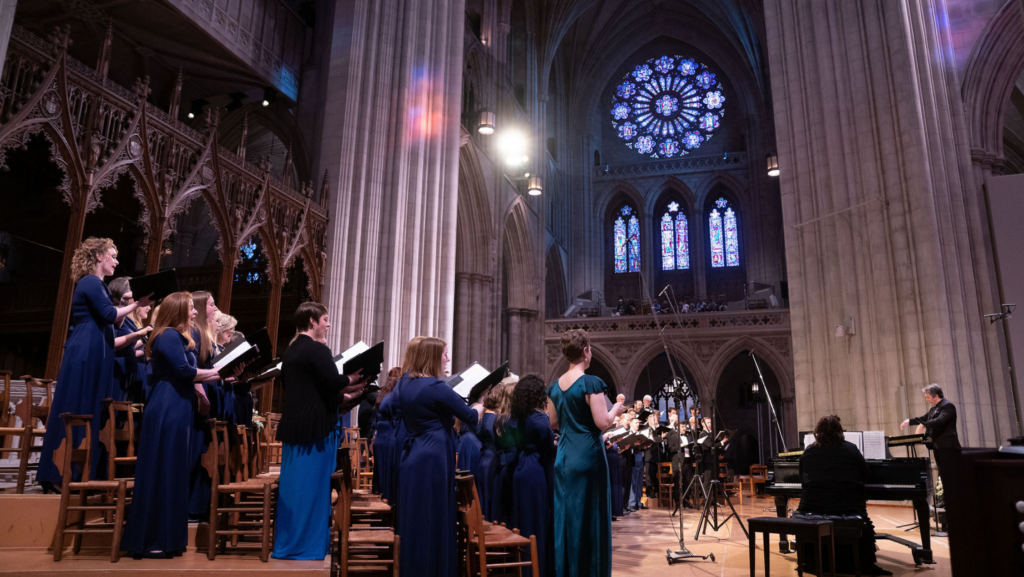 Cathedral Choral Society performs under the beautiful rose window at Washington National Cathedral with colorful light reflecting on the wall.